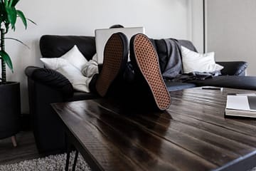 Un homme sur son ordi, assis sur son fauteuil confortablement avec les pieds sur la table basse